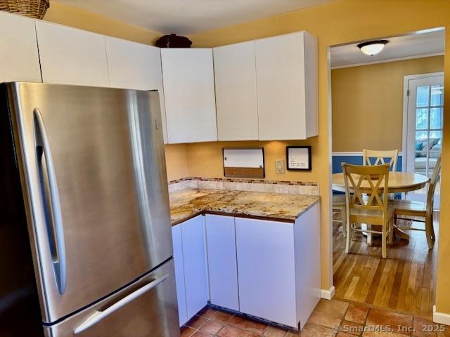 kitchen featuring white cabinets, freestanding refrigerator, and light stone counters