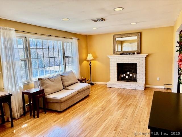 living area featuring light wood-style flooring, a fireplace, baseboards, and visible vents