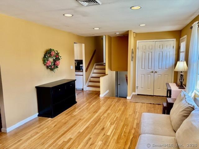 living room featuring light wood-style flooring, baseboards, visible vents, and stairway