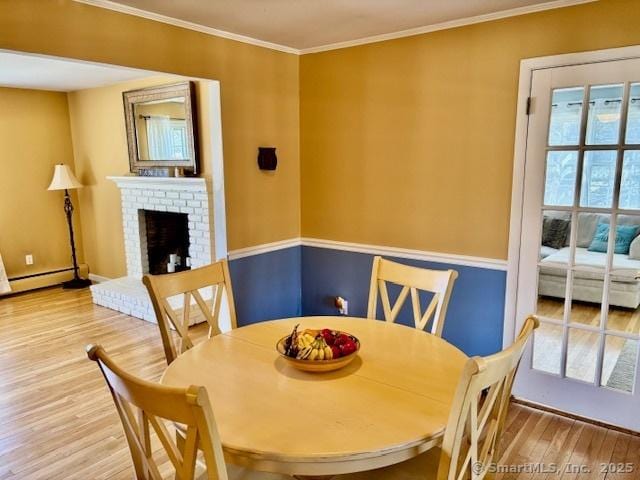 dining area with baseboards, a baseboard heating unit, ornamental molding, light wood-style floors, and a brick fireplace