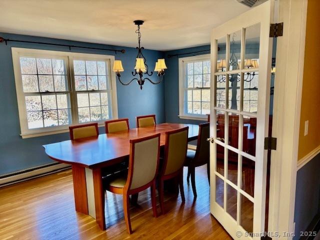dining space featuring a baseboard radiator, wood finished floors, and a notable chandelier