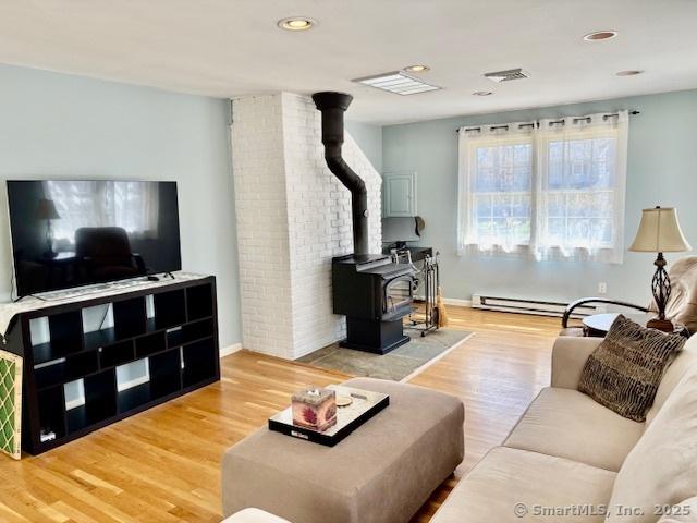 living area with visible vents, baseboards, a wood stove, recessed lighting, and wood finished floors