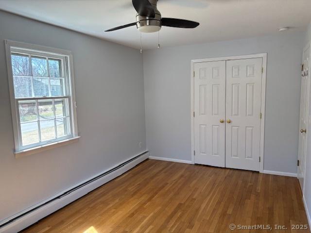 unfurnished bedroom with a baseboard radiator, a closet, wood finished floors, and baseboards