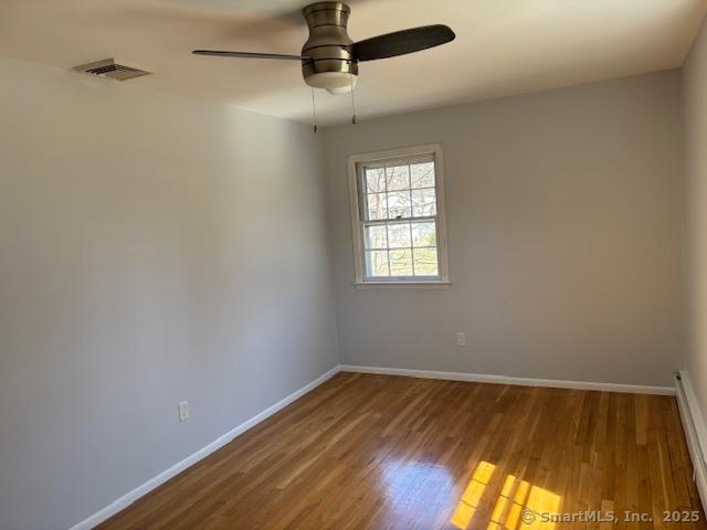 empty room with wood finished floors, ceiling fan, baseboards, and visible vents