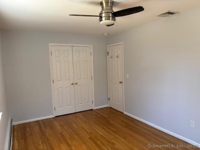 unfurnished bedroom featuring a closet, baseboards, visible vents, ceiling fan, and wood finished floors