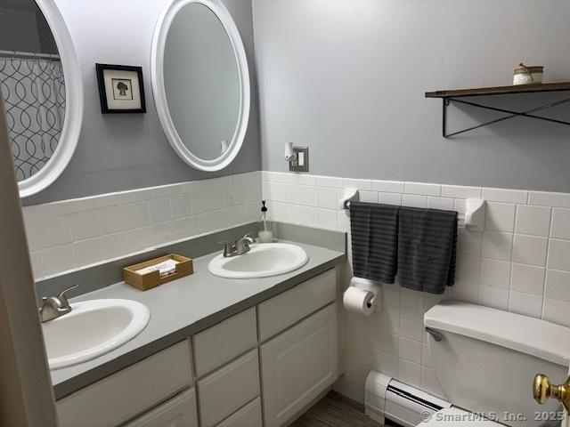 bathroom featuring a sink, tile walls, a baseboard radiator, and double vanity