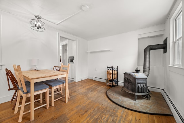 dining area featuring a wood stove, a notable chandelier, baseboard heating, and hardwood / wood-style flooring