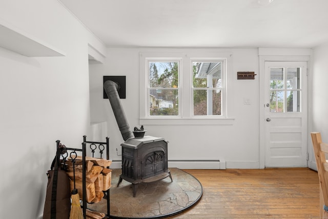 interior space with a healthy amount of sunlight, a baseboard heating unit, wood-type flooring, and a wood stove