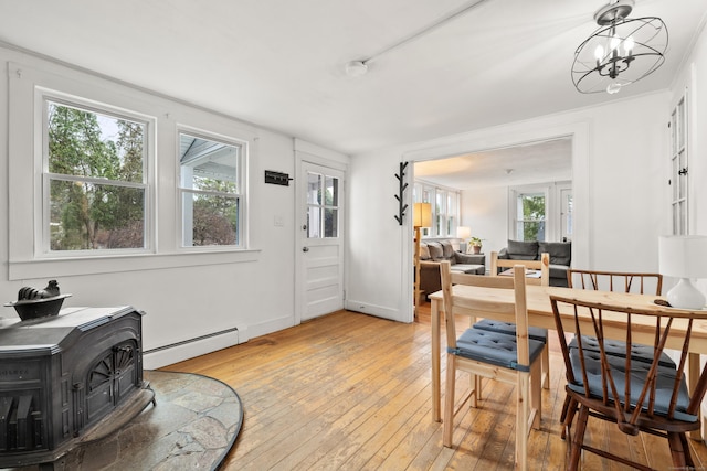dining room featuring a wood stove, light wood-type flooring, a baseboard heating unit, and baseboards