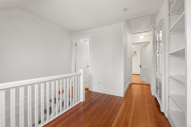 hallway with a baseboard heating unit, vaulted ceiling, baseboards, attic access, and wood-type flooring