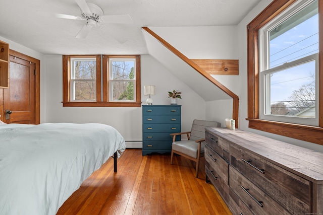 bedroom featuring ceiling fan, a baseboard heating unit, and light wood-style floors