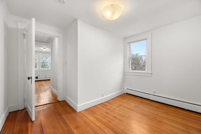 empty room featuring baseboards, a baseboard heating unit, ornamental molding, attic access, and light wood finished floors