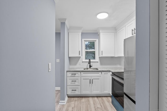 kitchen with light stone counters, light wood-style flooring, white cabinets, stainless steel appliances, and a sink
