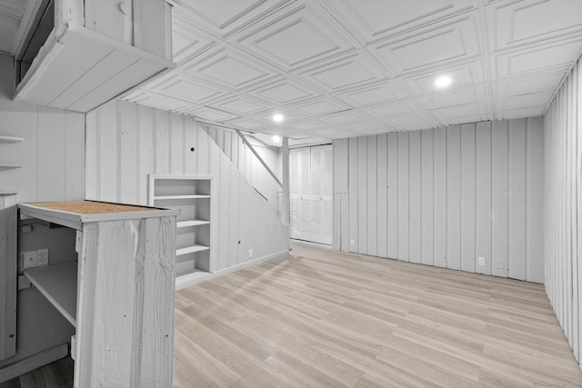 finished basement featuring wooden walls, an ornate ceiling, recessed lighting, and light wood-style floors