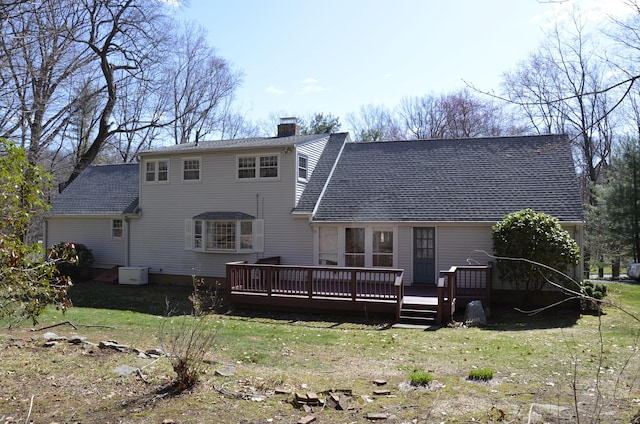 back of property with a chimney, a wooden deck, a shingled roof, and a lawn
