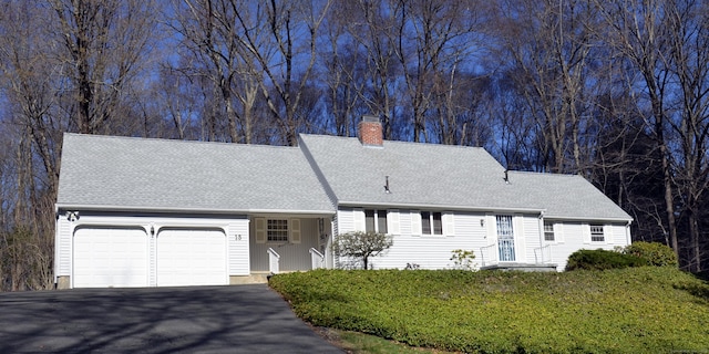 view of front of property featuring aphalt driveway, an attached garage, a front yard, a chimney, and a shingled roof