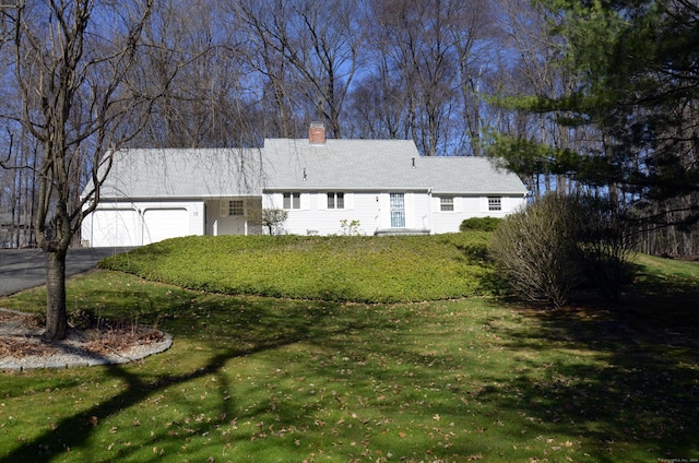 exterior space with an attached garage, a chimney, a front yard, and aphalt driveway