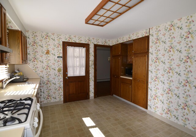 kitchen featuring baseboard heating, wallpapered walls, baseboards, a sink, and light countertops