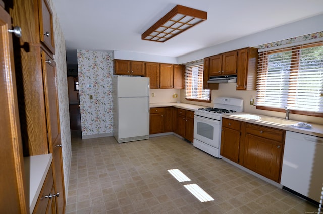 kitchen with light floors, white appliances, a sink, brown cabinets, and light countertops