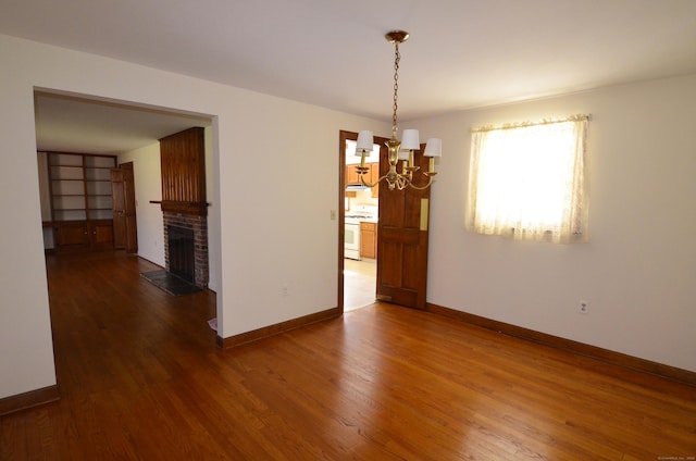 unfurnished dining area with baseboards, a fireplace, an inviting chandelier, and wood finished floors