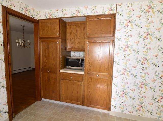 kitchen with wallpapered walls, brown cabinetry, stainless steel microwave, a baseboard heating unit, and a chandelier