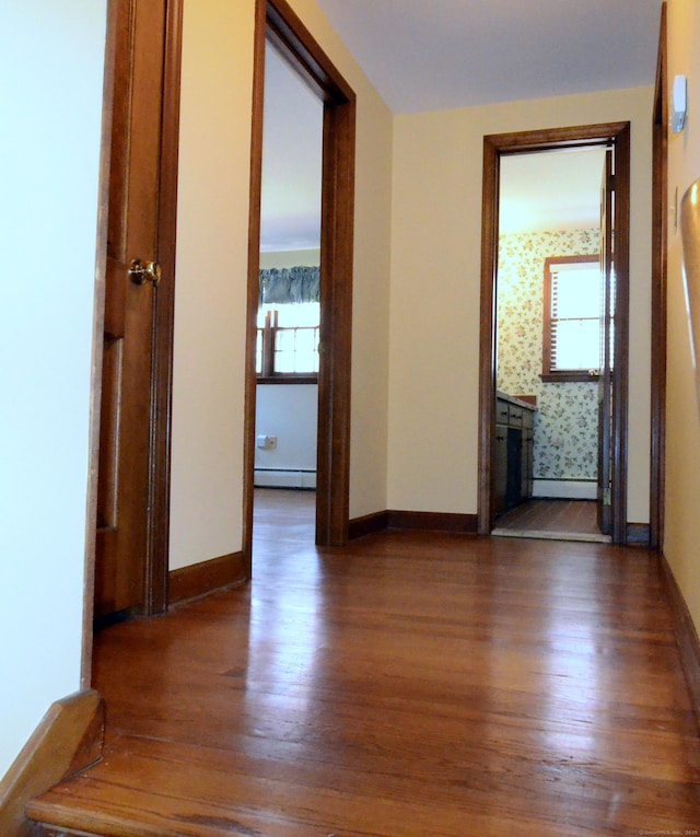 hallway featuring wood finished floors, baseboards, plenty of natural light, and a baseboard heating unit