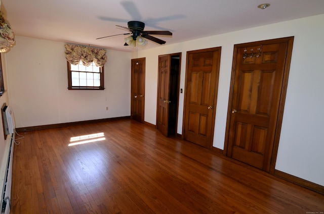 unfurnished bedroom featuring wood finished floors, baseboards, a ceiling fan, and multiple closets