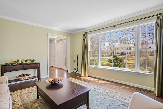 living area with baseboards, wood finished floors, visible vents, and crown molding
