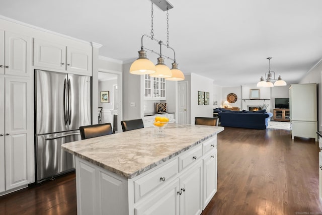 kitchen with dark wood-type flooring, freestanding refrigerator, light stone countertops, a kitchen island, and crown molding