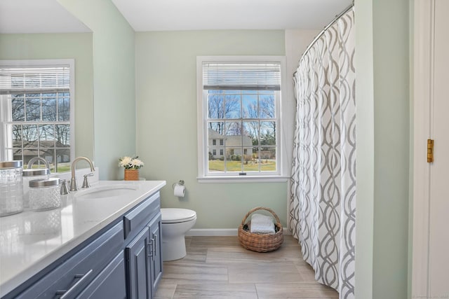 bathroom with baseboards, a wealth of natural light, toilet, and vanity
