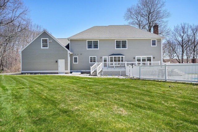 back of property with a lawn, a chimney, fence, a wooden deck, and roof with shingles