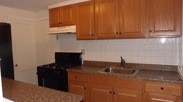kitchen with under cabinet range hood, backsplash, dark countertops, a sink, and black appliances