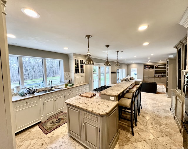 kitchen with a sink, stainless steel gas stovetop, open floor plan, light stone countertops, and a kitchen island