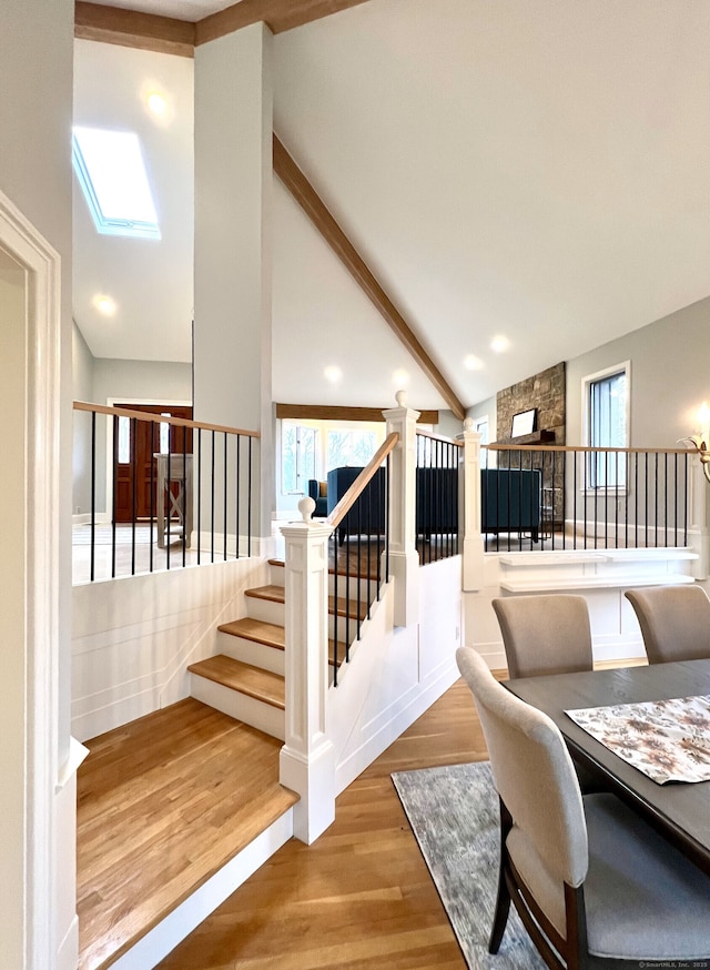 living area with high vaulted ceiling, stairs, wood finished floors, a skylight, and beamed ceiling