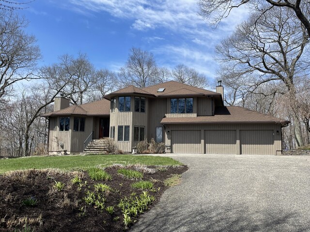 prairie-style home with a front lawn, roof with shingles, a chimney, and aphalt driveway