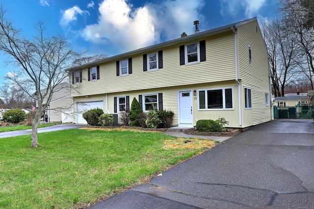 colonial home with asphalt driveway, a front lawn, a garage, and a chimney