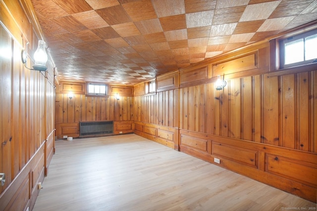 basement with plenty of natural light, wood walls, radiator heating unit, and wood finished floors