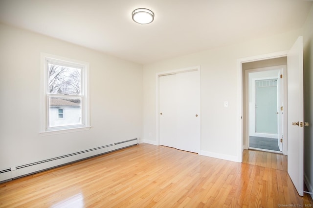 unfurnished bedroom featuring a closet, light wood-style flooring, baseboards, and baseboard heating