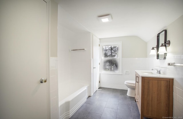 full bathroom with tile walls, vaulted ceiling, vanity, tile patterned floors, and toilet