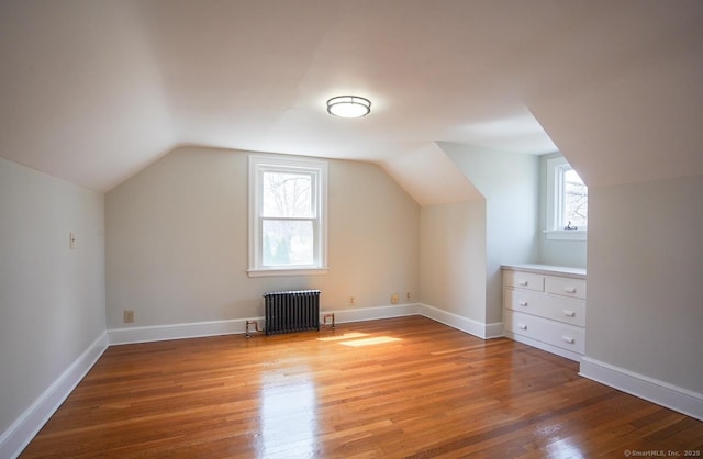 additional living space with baseboards, lofted ceiling, radiator, and light wood-style floors