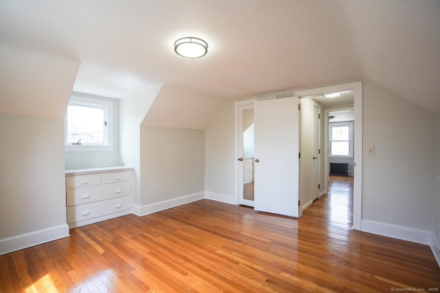 additional living space with baseboards, vaulted ceiling, and light wood-style floors