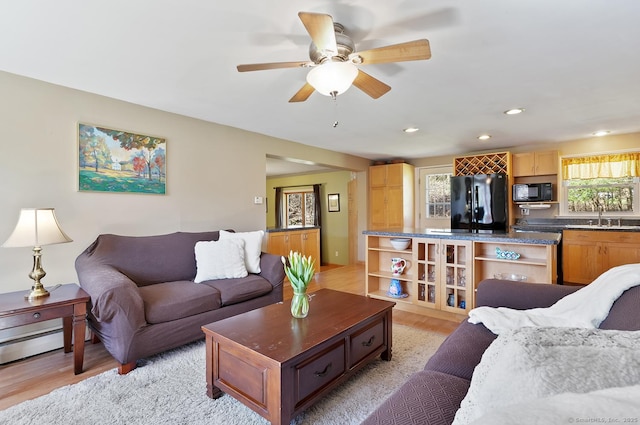 living area with light wood-style flooring, a baseboard heating unit, a ceiling fan, and recessed lighting