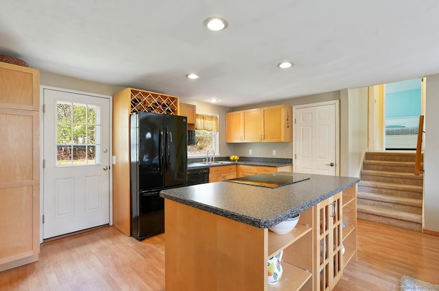 kitchen featuring dark countertops, black appliances, light wood-style floors, a sink, and light brown cabinetry