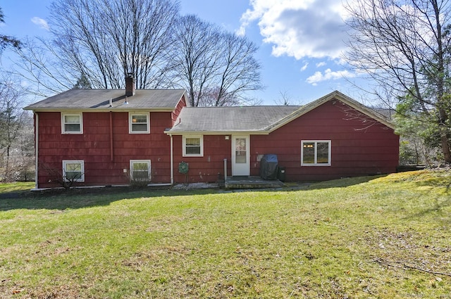 rear view of house with a chimney, a shingled roof, and a lawn