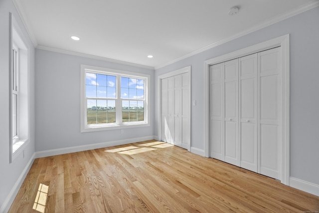 unfurnished bedroom featuring crown molding, baseboards, two closets, and light wood-style floors