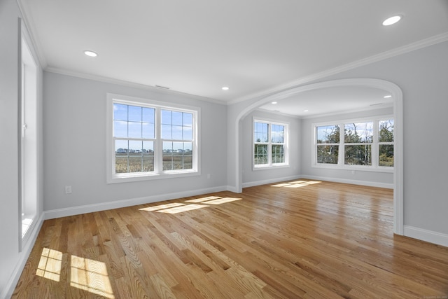 unfurnished living room featuring arched walkways, light wood-style flooring, baseboards, and crown molding