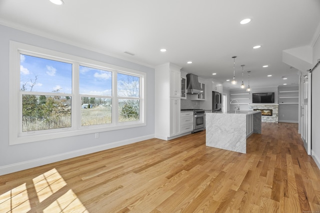 kitchen with wall chimney range hood, open floor plan, a center island with sink, visible vents, and appliances with stainless steel finishes