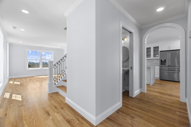 hallway with crown molding, stairs, arched walkways, light wood finished floors, and baseboards