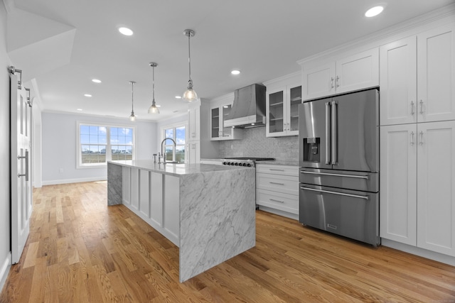 kitchen featuring tasteful backsplash, wall chimney range hood, high quality fridge, white cabinetry, and light stone counters