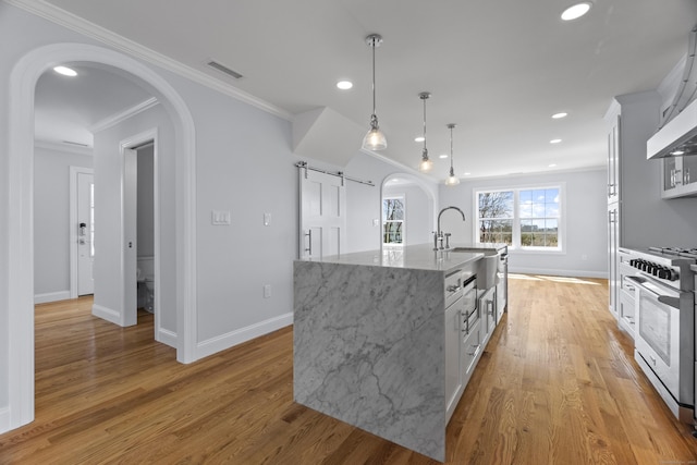 kitchen with crown molding, an island with sink, arched walkways, visible vents, and stainless steel gas range oven